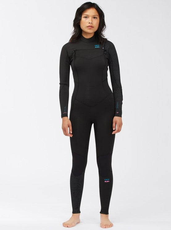 A woman standing straight facing forward, wearing a Billabong wetsuit with a chest zip entry. The wetsuit is black with the brand logo visible on the upper chest area.