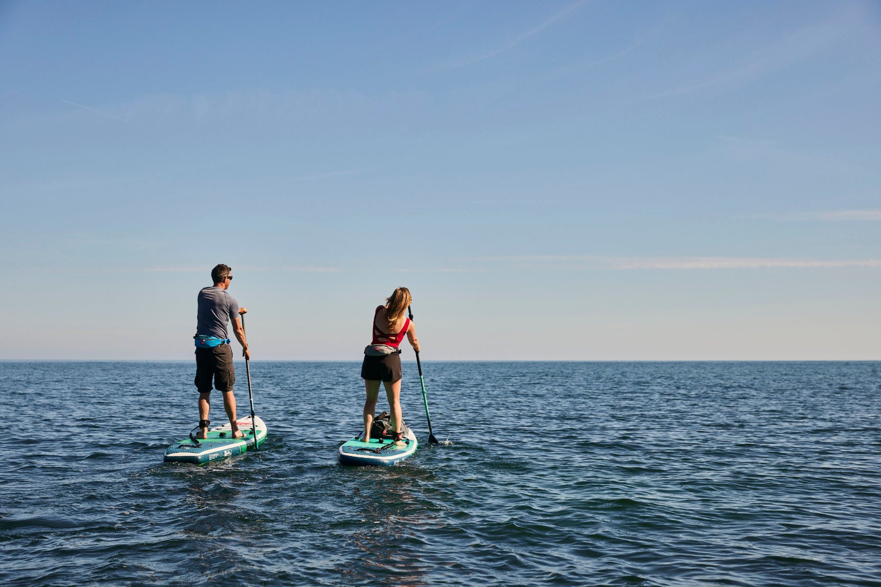 A couple paddle boarding in the sea wearing Red Paddle safety equipment