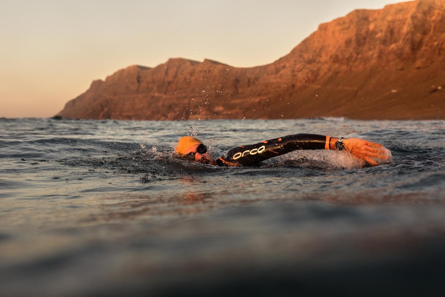 man swimming in the sea at sun rise with cliffs in the background