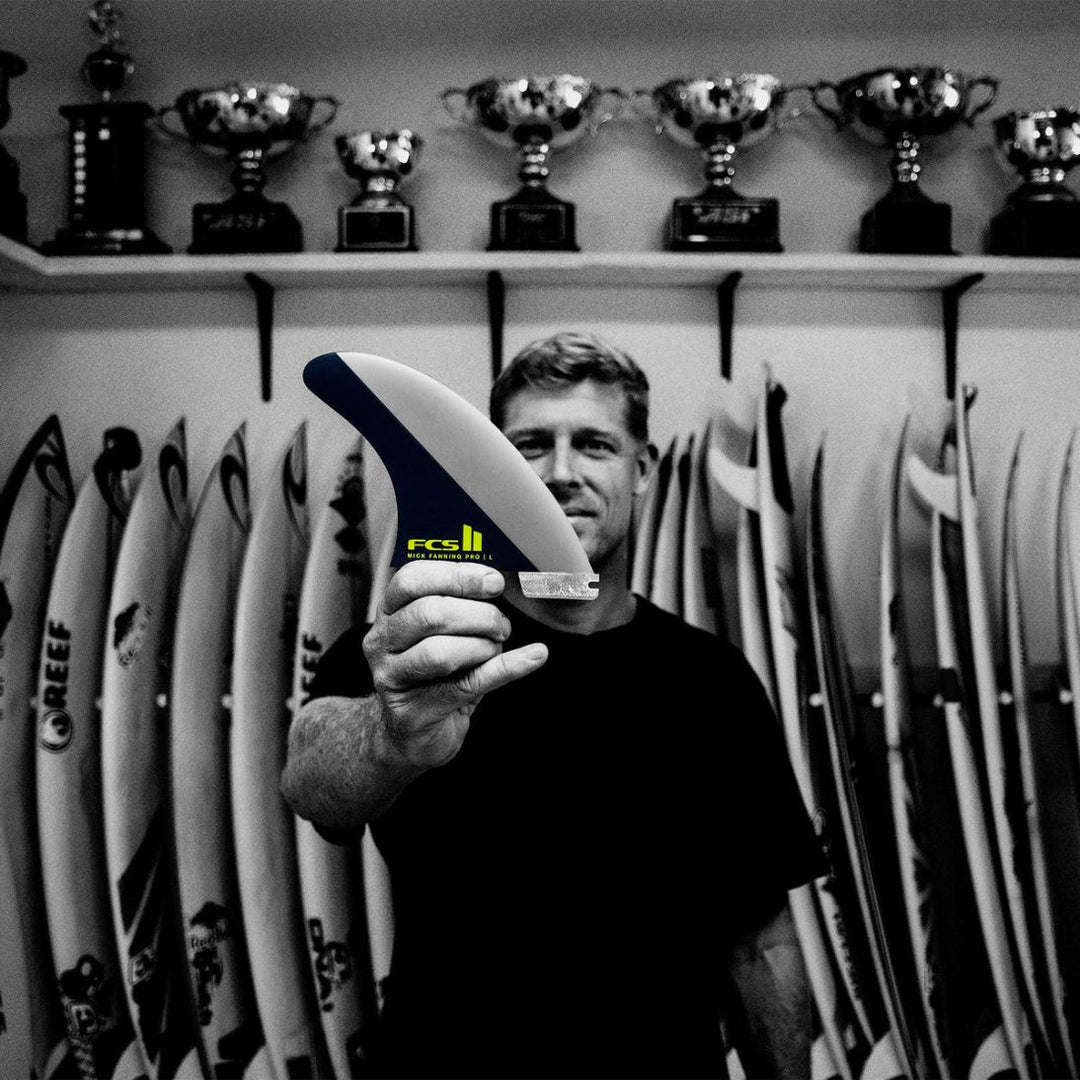 Mick Fanning holding a surf fin with trophies on shelves in the background