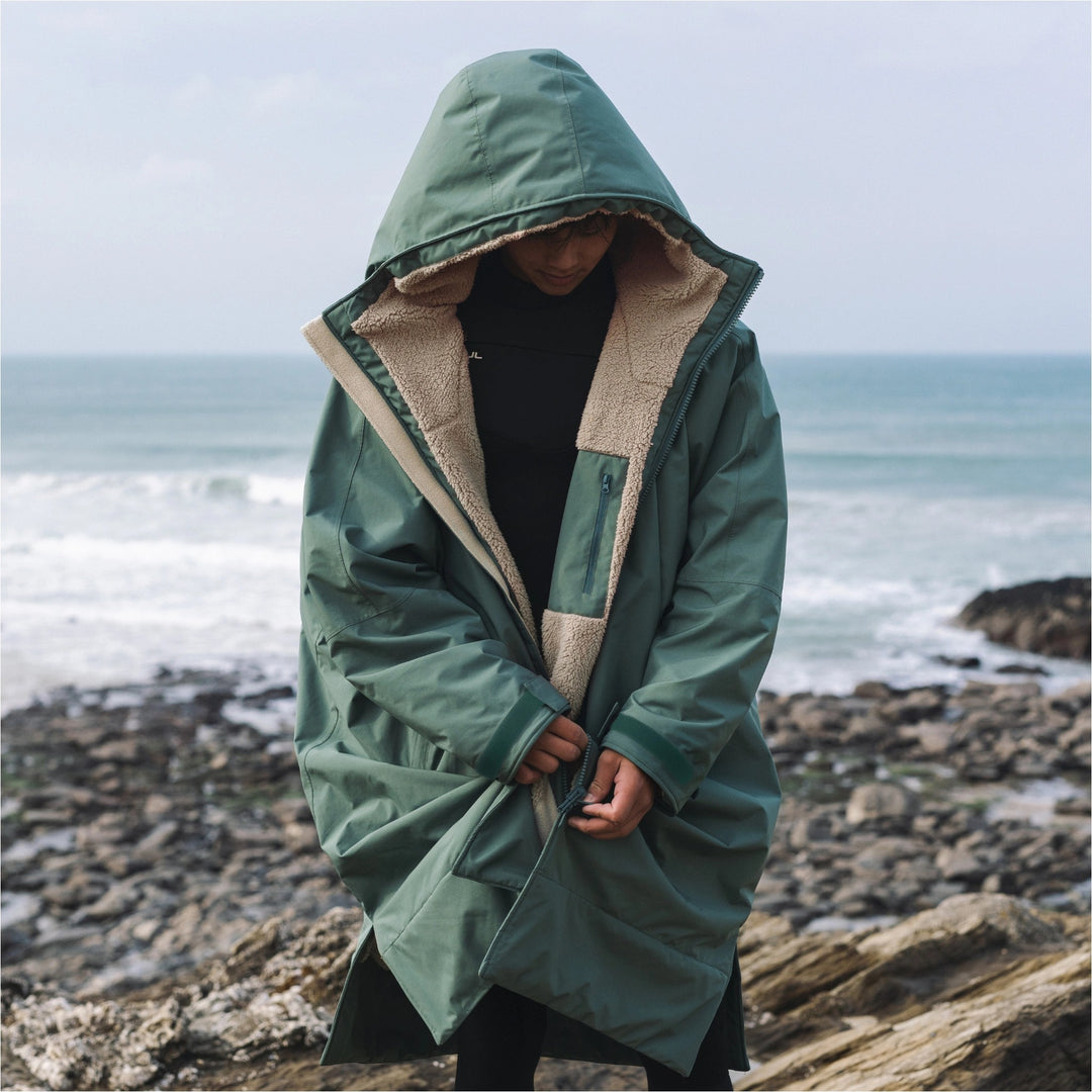 Surfer wearing the green Gul Revorobe with hood up, showing the sherpa lining