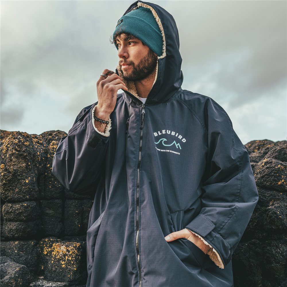 A man wearing a long-sleeved navy-colored Bleubird Nordic outdoor changing robe with a hood