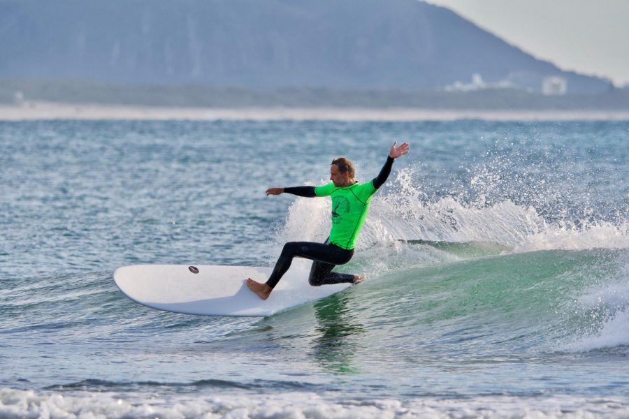 A man in a bright green rash vest surfing a NSP Protech 9ft Longboard Surfboard
