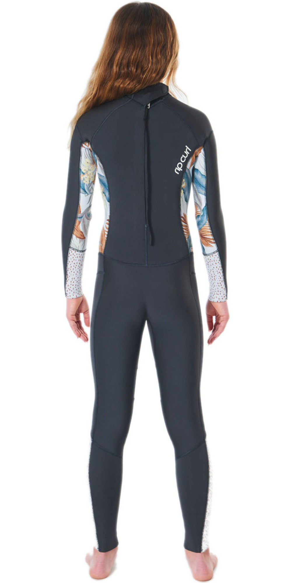 A girl wearing a black and multicolored floral Rip Curl Dawn Patrol 5mm kids wetsuit with a back zip. View of the back.